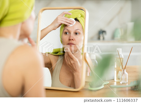 Woman with towel on head removing makeup with cotton pads Woman with towel on head removing makeup with cotton pads 111606337