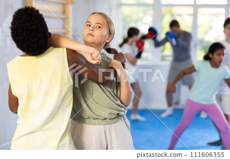 Girl practicing armlock with elbow strike to chin in mock bout with boy 111606355