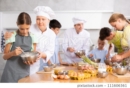 Tween girl mixing sauce under guidance of female chef during cooking masterclass 111606361