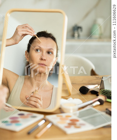 Middle-aged woman applying liquid foundation on her face Middle-aged woman applying liquid foundation on her face 111606629