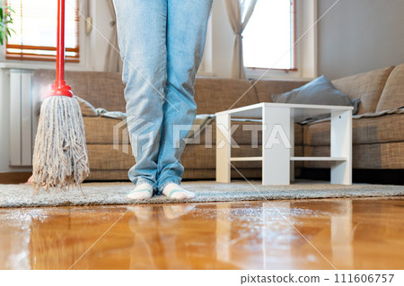 Person holds mop, close-up of parquet floor and legs. Low angle view. Copy space. Cleaning service and chores Person holds mop, close-up of parquet floor and legs. Low angle view. Copy space. Cleaning service and chores 111606757