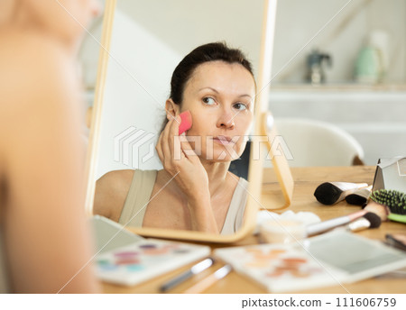 Woman applying foundation with makeup sponge in front of mirror Woman applying foundation with makeup sponge in front of mirror 111606759