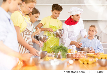 Group of teenagers and friendly chef cook cooking in modern kitchen. Learn to beat raw eggs 111606888