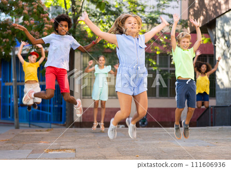 Cheerful preteen girl jumping with friends on summer city street 111606936