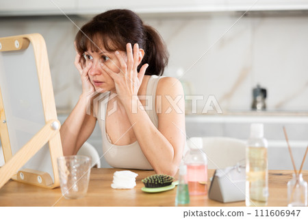 Woman inspecting facial skin in mirror during daily routine Woman inspecting facial skin in mirror during daily routine 111606947