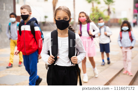 Schoolgirl in mask standing near school, children on background 111607172