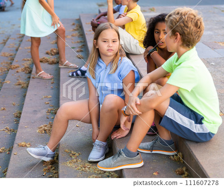 Cheerful preteen girls and boys sitting on steps outdoors and chatting 111607278