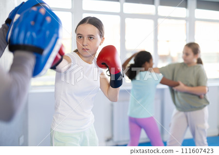 Focused girl hitting the focus mitts held by his boxing trainer in gym Focused girl hitting the focus mitts held by his boxing trainer in gym 111607423