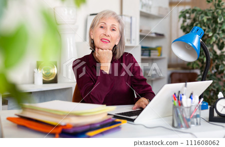 Smiling aged businesswoman posing at workplace during working day 111608062