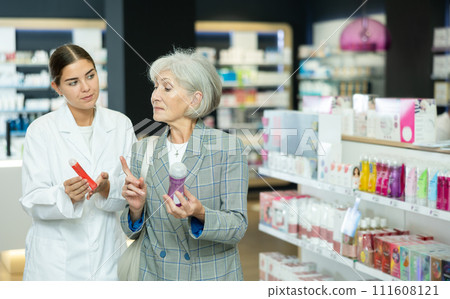 Girl pharmacist helps senior woman buyer to decide on choice of lubricant. 111608121