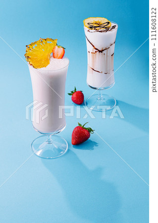 two glass cups of milkshake with dry pineapple and strawberries 111608122