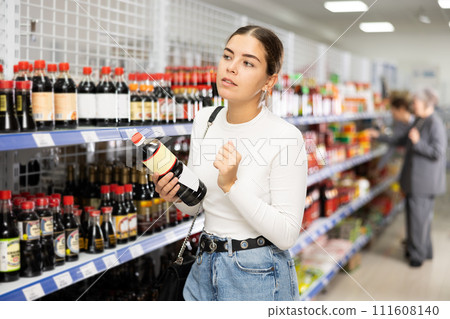 Girl customer is thinking about buying spicy and unusual soy sauce. 111608140