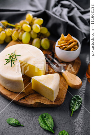 Round cheese on a wooden board and green grapes 111608158