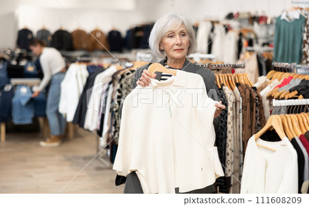 Elderly woman chooses coat in store 111608209
