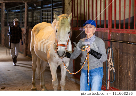 Mature woman with a white horse in stable Mature woman with a white horse in stable 111608256