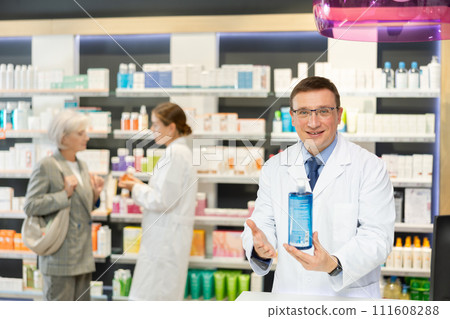 Positive male pharmacist in medical uniform posing with intimate hygiene product in hands in pharmacy 111608288