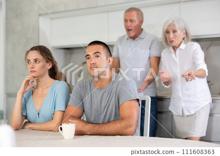 Portrait of an offended married couple in home kitchen, which mature family members reprimand. Family conflict 111608363
