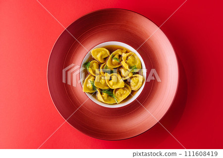 Filled tortellini with herbs on red plate Filled tortellini with herbs on red plate 111608419