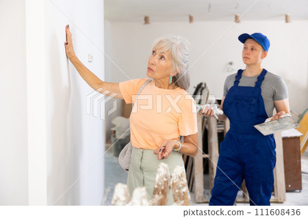 Mature woman checks the quality of plastered wall in room being renovated 111608436
