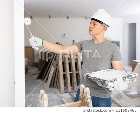 Teenage boy painting wall with roller during his workday on first job 111608463