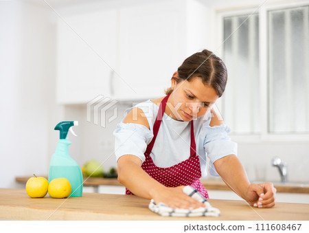young woman wiping dust from kitchen surfaces with cleaning rag and detergent spray 111608467