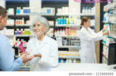 Mature female pharmacist consulting middle-aged man costumer about care product in box 111608468