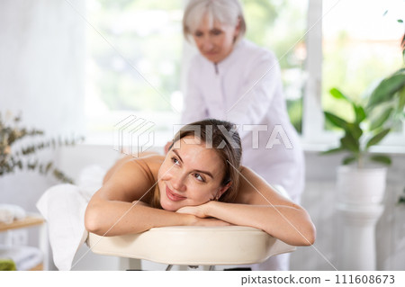 Vague mature woman actively rubs buttocks of young woman during general massage procedure. Vague mature woman actively rubs buttocks of young woman during general massage procedure. 111608673