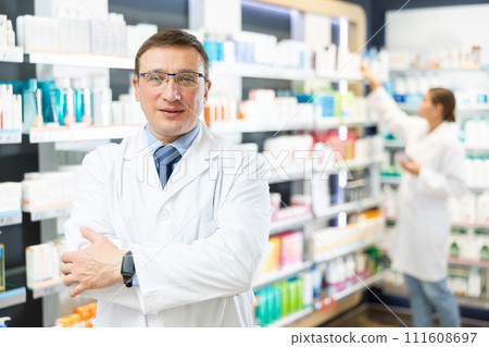 Middle-aged male pharmacist posing in chemist's shop with large assortment Middle-aged male pharmacist posing in chemist's shop with large assortment 111608697