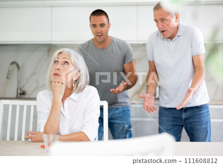 Elderly and adult man quarreling with elderly woman in kitchen Elderly and adult man quarreling with elderly woman in kitchen 111608812