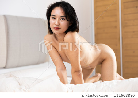 Naked Asian woman is on all fours on unmade bed. 111608880