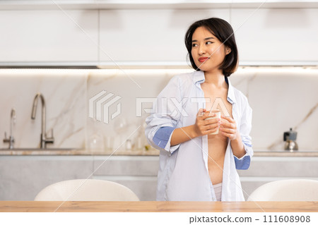 In kitchen, semi naked Asian woman in lady underpants and dressing-gown stands by table In kitchen, semi naked Asian woman in lady underpants and dressing-gown stands by table 111608908