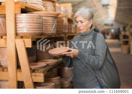 Aged woman choosing earthenware crockery in store 111609001