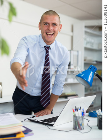 Positive European man office manager reaching out his hand for handshake and looking in camera. 111609141