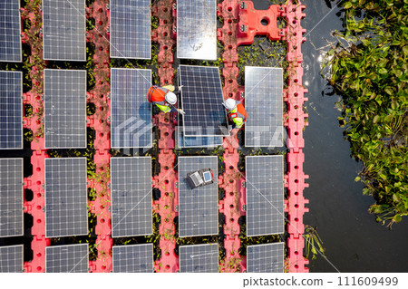 Close up and top view of two technician workers set up or install solar cell panel over the water reservoir as solar farm factory in concept of green energy for good environment. Close up and top view of two technician workers set up or install solar cell panel over the water reservoir as solar farm factory in concept of green energy for good environment. 111609499