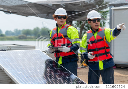 Two technician workers with safety uniform stand beside of solar cell panel and one point forward to discuss about work with his co-worker in workplace. Two technician workers with safety uniform stand beside of solar cell panel and one point forward to discuss about work with his co-worker in workplace. 111609524