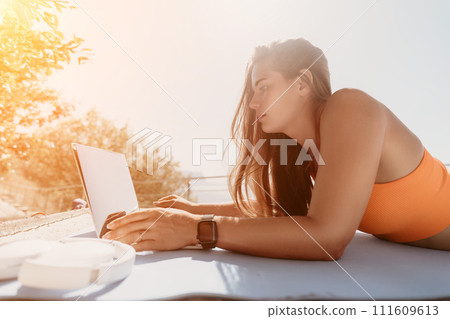 Woman laptop sea. Working remotely on seashore. Happy successful woman female freelancer working on laptop by the sea at sunset, makes a business transaction online. Freelance, remote work on vacation Woman laptop sea. Working remotely on seashore. Happy successful woman female freelancer working on laptop by the sea at sunset, makes a business transaction online. Freelance, remote work on vacation 111609613