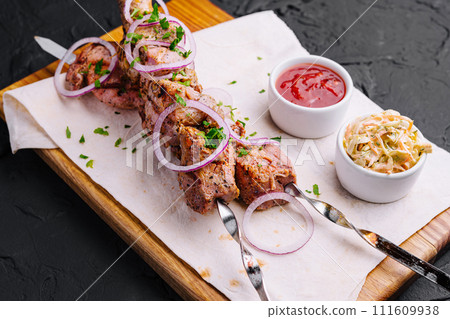Juicy kebabs from pork on skewers laid out on a decorative board Juicy kebabs from pork on skewers laid out on a decorative board 111609938