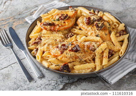 American Marry Me Chicken pasta with sun-dried tomatoes, cheese, herbs and aromatic creamy sauce close-up in a plate. Horizontal American Marry Me Chicken pasta with sun-dried tomatoes, cheese, herbs and aromatic creamy sauce close-up in a plate. Horizontal 111610316