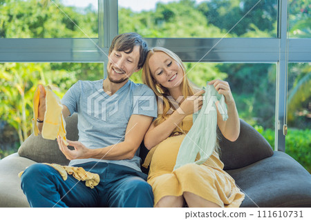 In a heartwarming scene, the future mom and dad hold their unborn baby's clothes in their hands, savoring the joy of anticipation and shared excitement for their little one's arrival In a heartwarming scene, the future mom and dad hold their unborn baby's clothes in their hands, savoring the joy of anticipation and shared excitement for their little one's arrival 111610731