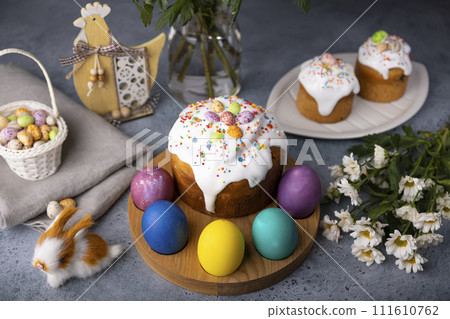 Easter kulich with candied fruits in white glaze with colorful sprinkles and painted eggs. Traditional Easter pastry. Easter holiday. Close-up, selective focus. Easter kulich with candied fruits in white glaze with colorful sprinkles and painted eggs. Traditional Easter pastry. Easter holiday. Close-up, selective focus. 111610762