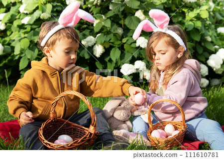 Little boy and girl in bunny ears with baskets with eggs at traditional Easter holiday on sunny day Little boy and girl in bunny ears with baskets with eggs at traditional Easter holiday on sunny day 111610781
