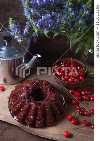 Delicious chocolate cake with sweet cherry, vintage kettle and bouquet of blue flowers on dark wooden background.. 111611265