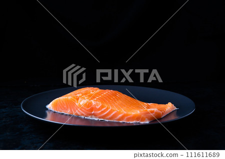Raw salmon filet with rosemary and spices on plate, black stone background. Top view, flat lay 111611689