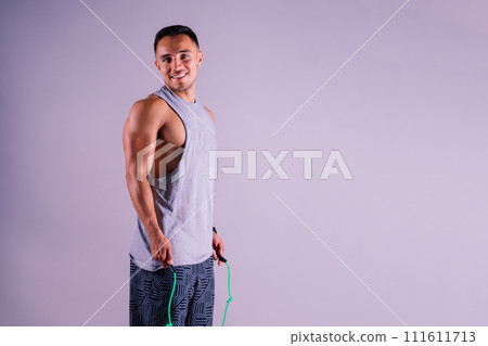 Young man exercising with a skipping rope and looking at the camera isolated on grey background 111611713