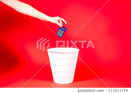 A hand throws a tax calculator into trash. The calculator is thrown into the office wastebasket. A hand throws a tax calculator into trash. The calculator is thrown into the office wastebasket. 111611734