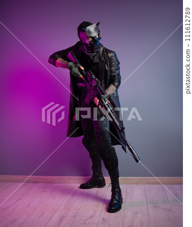 A tough guy killer in a demon mask and black raincoat with a sniper airsoft rifle in his hands A tough guy killer in a demon mask and black raincoat with a sniper airsoft rifle in his hands 111612789