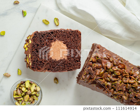 Travel Cake or Tube Cake or Voyage Cake filled center tube ganache and topped chocolate icing and pistachio. Chocolate loaf cake with chocolate cream-cheese filled center. Top view or flat lay Travel Cake or Tube Cake or Voyage Cake filled center tube ganache and topped chocolate icing and pistachio. Chocolate loaf cake with chocolate cream-cheese filled center. Top view or flat lay 111614914