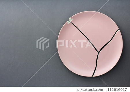 A broken pink ceramic plate on a gray background. view from above. The concept of diet, old things A broken pink ceramic plate on a gray background. view from above. The concept of diet, old things 111616017