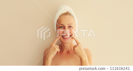 Happy smiling middle-aged woman points to her white clean teeth drying her wet hair Happy smiling middle-aged woman points to her white clean teeth drying her wet hair 111616241