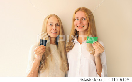 Portrait of happy smiling middle aged mother and adult daughter holding plastic credit bank card Portrait of happy smiling middle aged mother and adult daughter holding plastic credit bank card 111616309